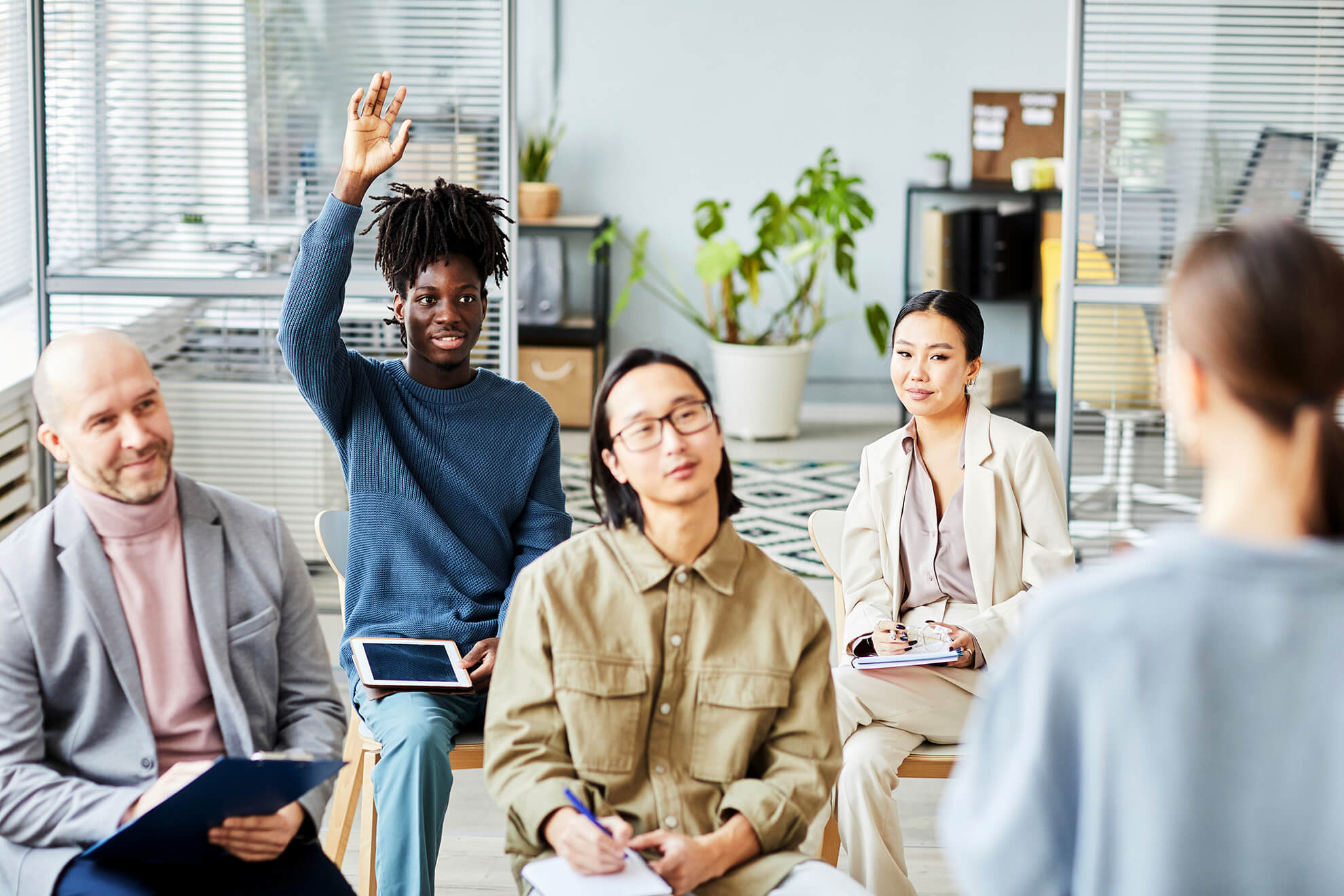 Young male employee raises hand for question during a workplace training course in office